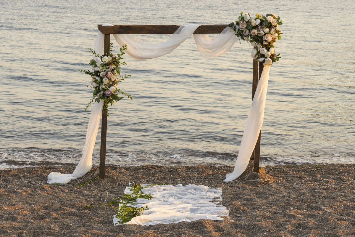 Draped wooden ceremony arch with flowers on a beach at the water's edge