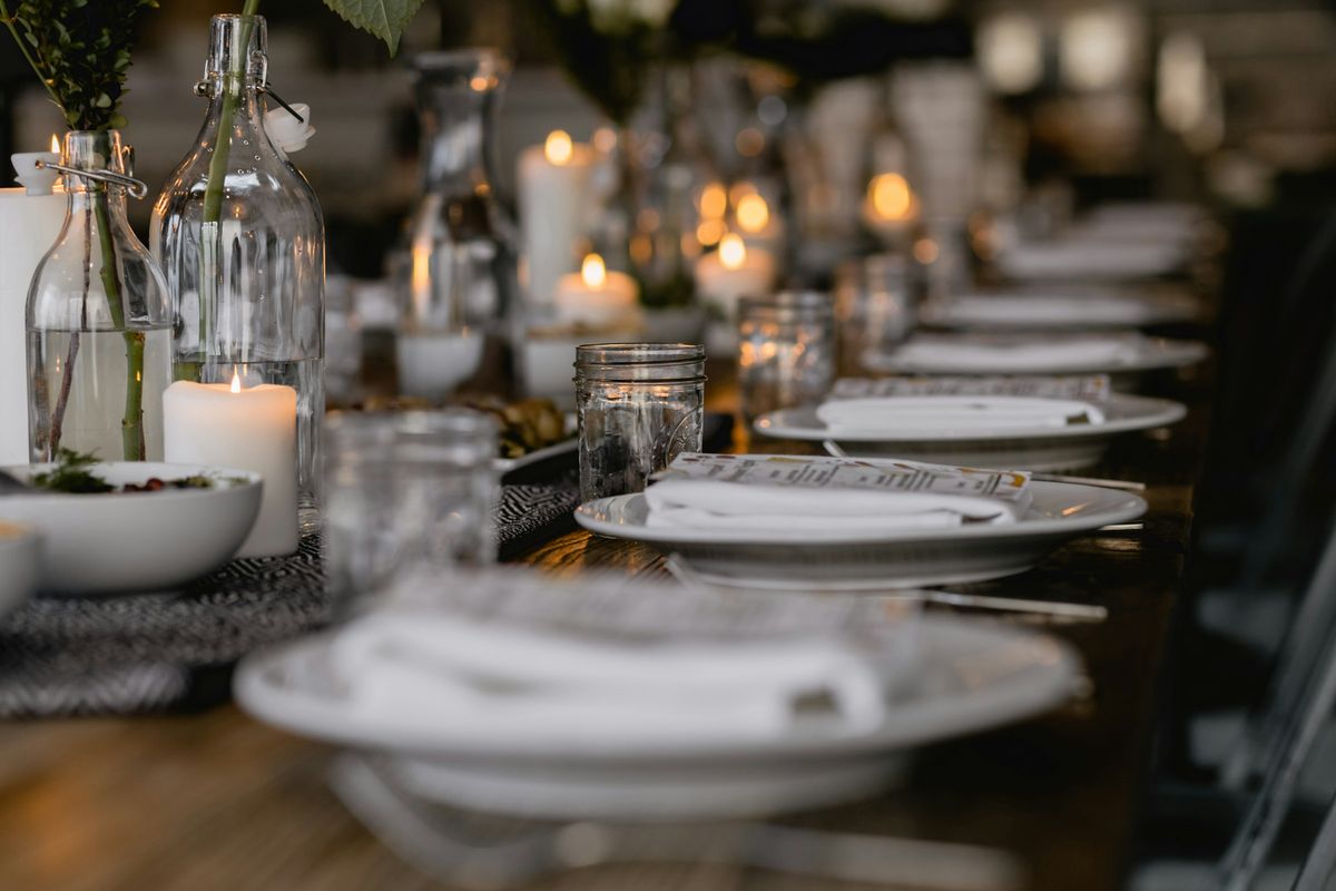 Candlelit long dinner table set with white plates and glassware