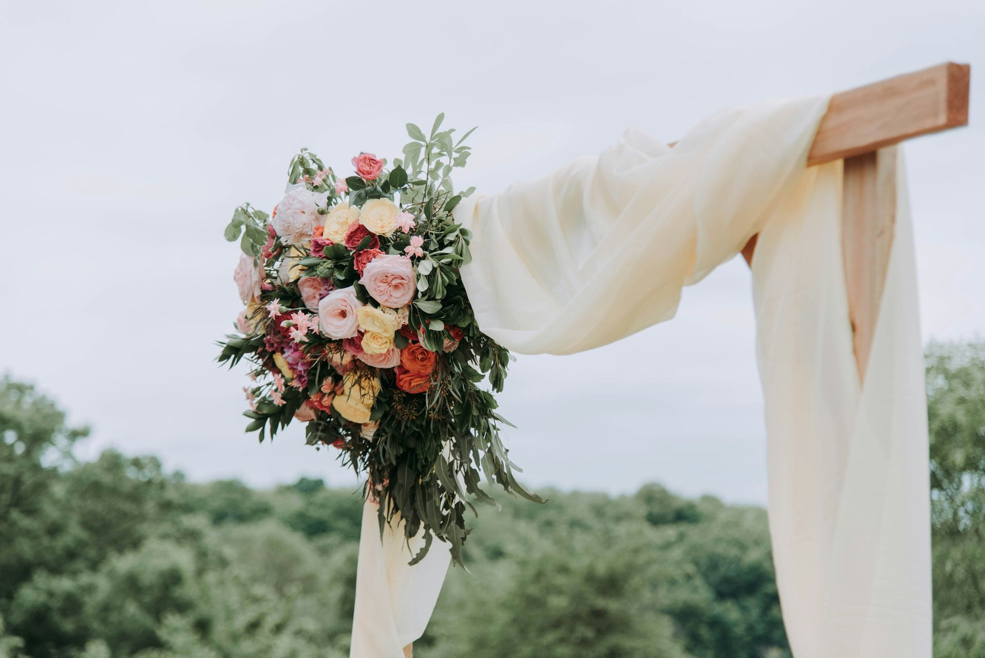 Ceremony arch draped in white fabric with a pink and cream floral bouquet