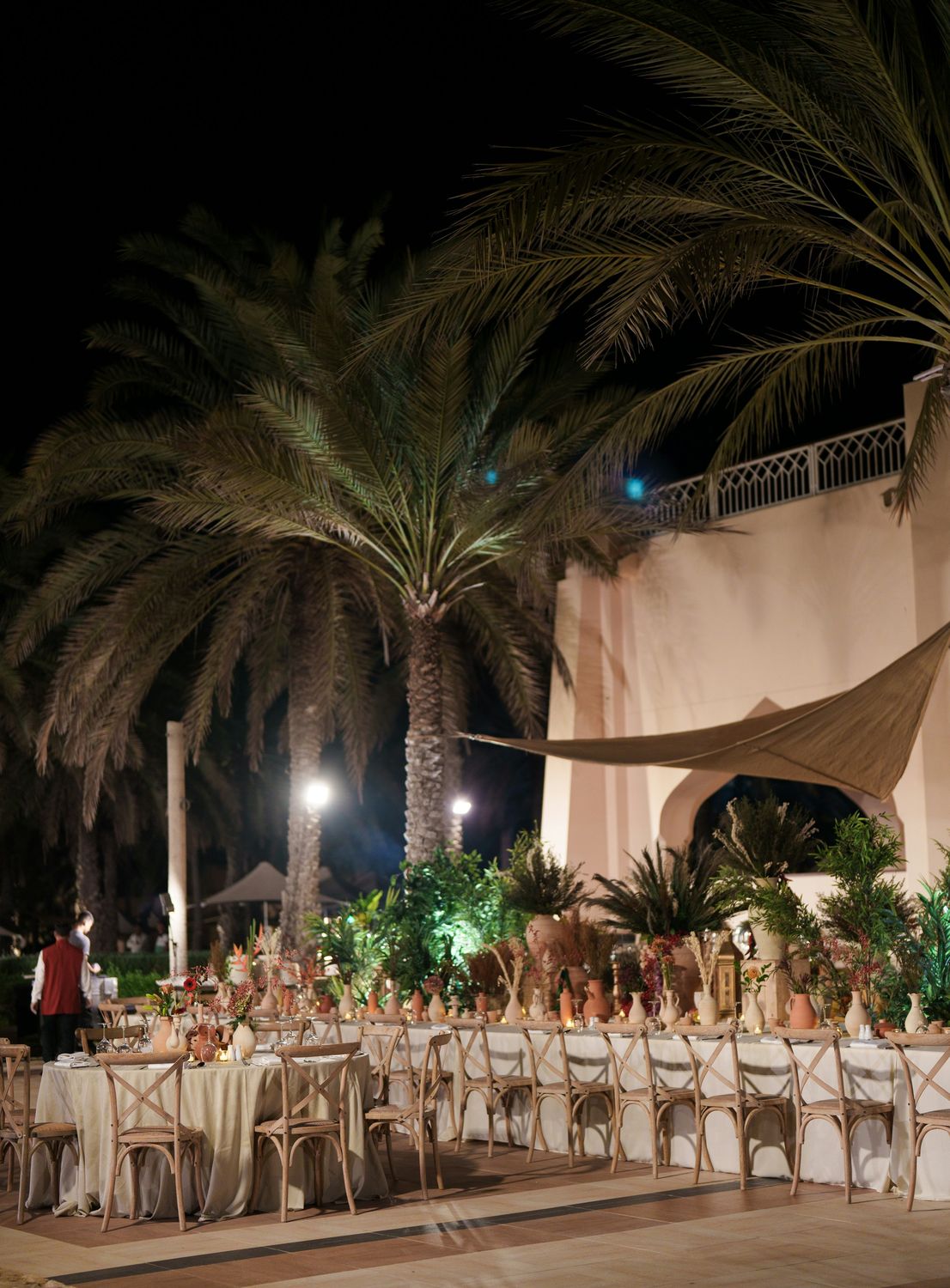 Long outdoor dinner tables under palm trees at night