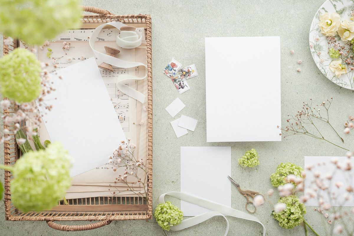 Planning flat lay with blank cards, ribbon, scissors and pale green flowers